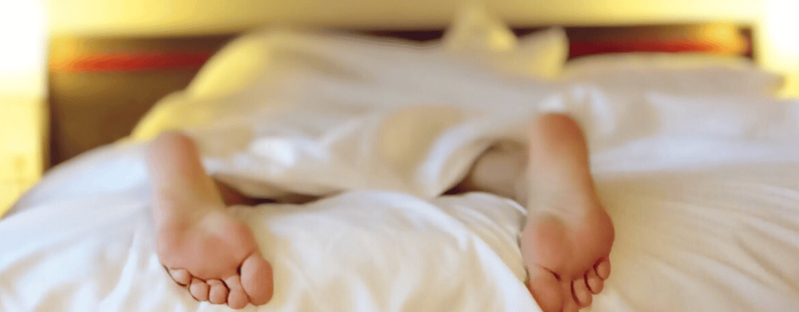stopy śpiącej osoby wystające spod kołdry o poranku